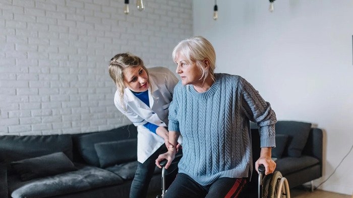 Caregiver assisting elderly woman walking with walker